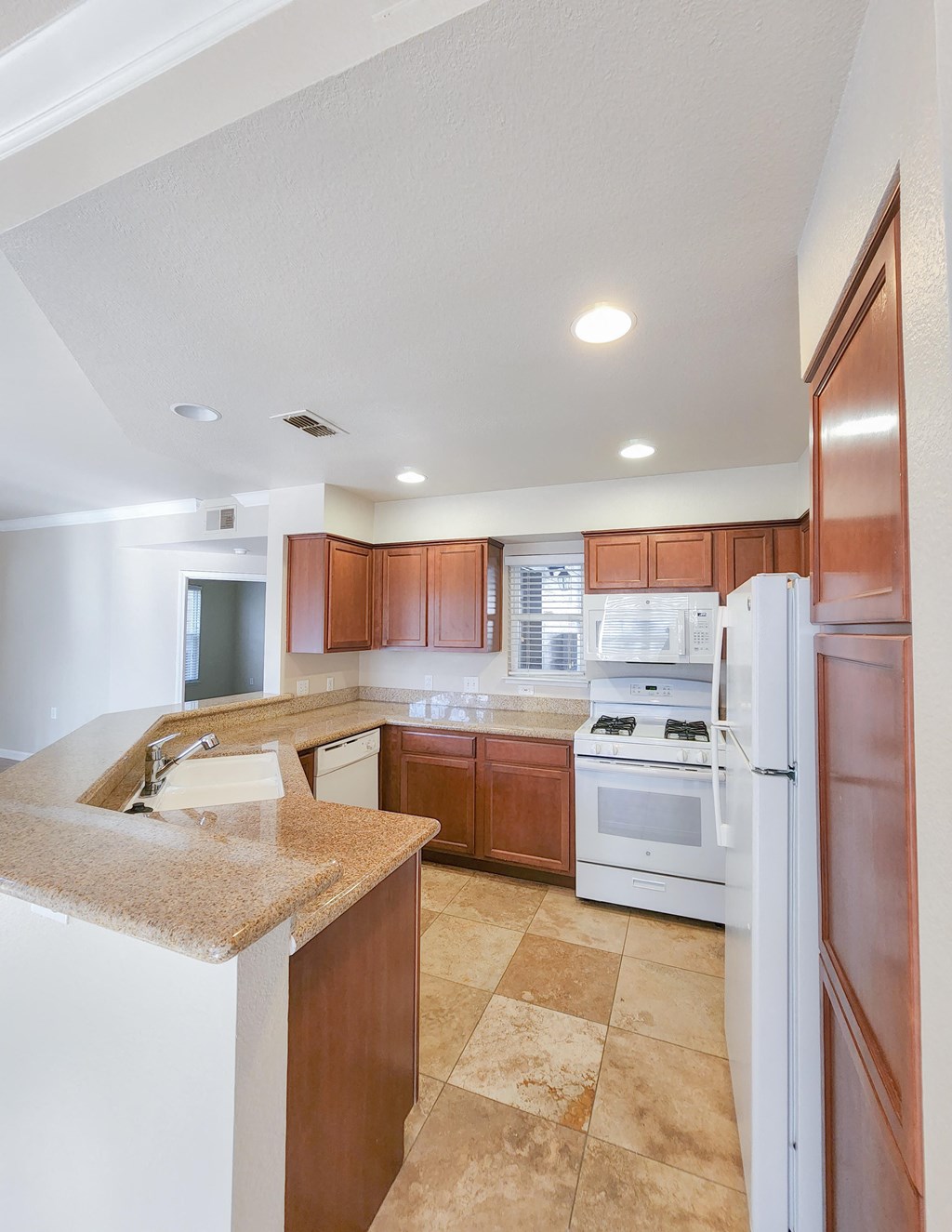 View of kitchen with brown cabinets, white appliances, stone counters, tile flooring, and recessed lighting