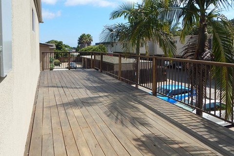 A wooden deck with a pool and palm trees in the background.