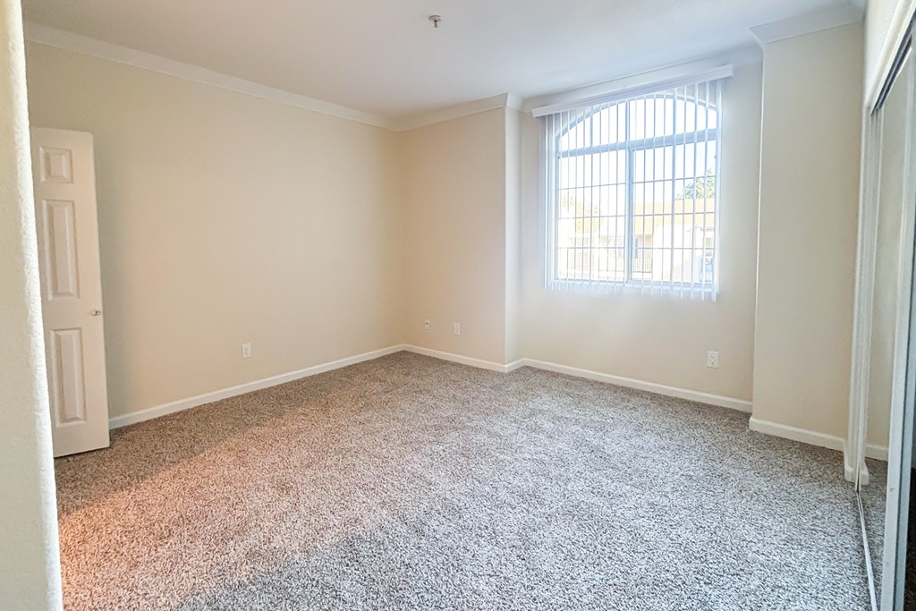 A room with a carpeted floor and a window with bars on it.