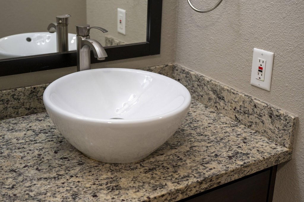 A white porcelain sink is placed on a granite countertop at Sierra Oaks Living Apartments, Cameron Park