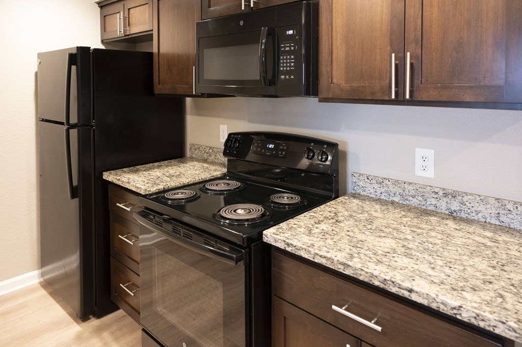 A black refrigerator and stove in a kitchen with granite countertops at Sierra Oaks Living Apartments, California 95682