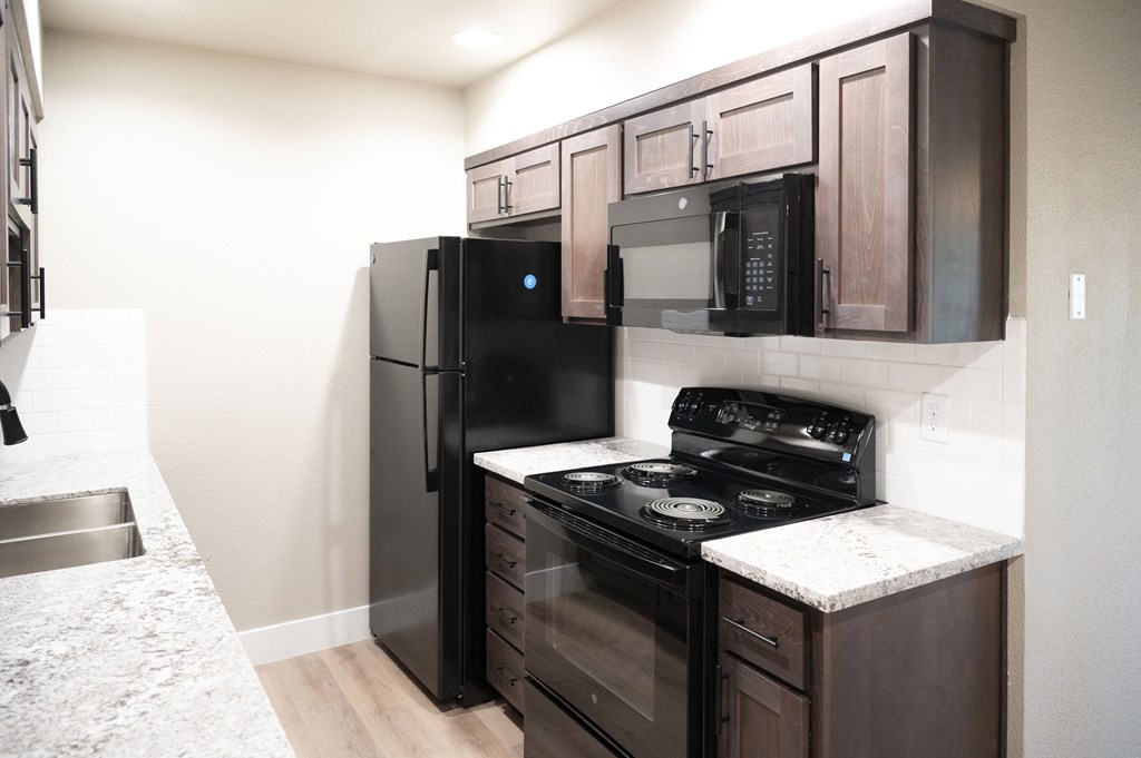 A black refrigerator and microwave in a kitchen with wooden cabinets at Sierra Oaks Living Apartments, California
