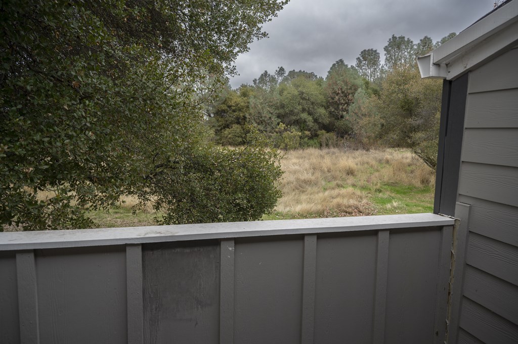 A grey fence with a view of a grassy field and trees in the distance at Sierra Oaks Living Apartments, Cameron Park, CA