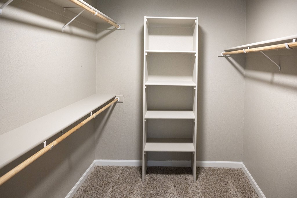 A room with a carpeted floor and a white wall with a shelf and a rack at Sierra Oaks Living Apartments, California