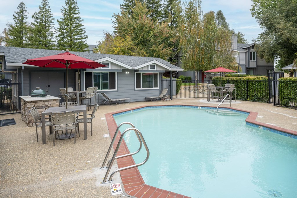 A pool with a red umbrella and a house in the background at Sierra Oaks Living Apartments, Cameron Park, CA