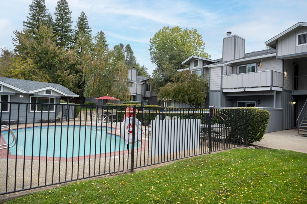 A black fence surrounds a small pool with a red umbrella at Sierra Oaks Living Apartments, California 95682
