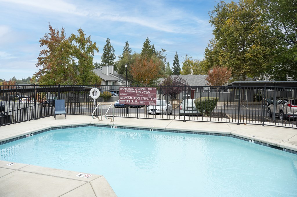 A pool surrounded by a black fence with a sign at Sierra Oaks Living Apartments, Cameron Park, CA