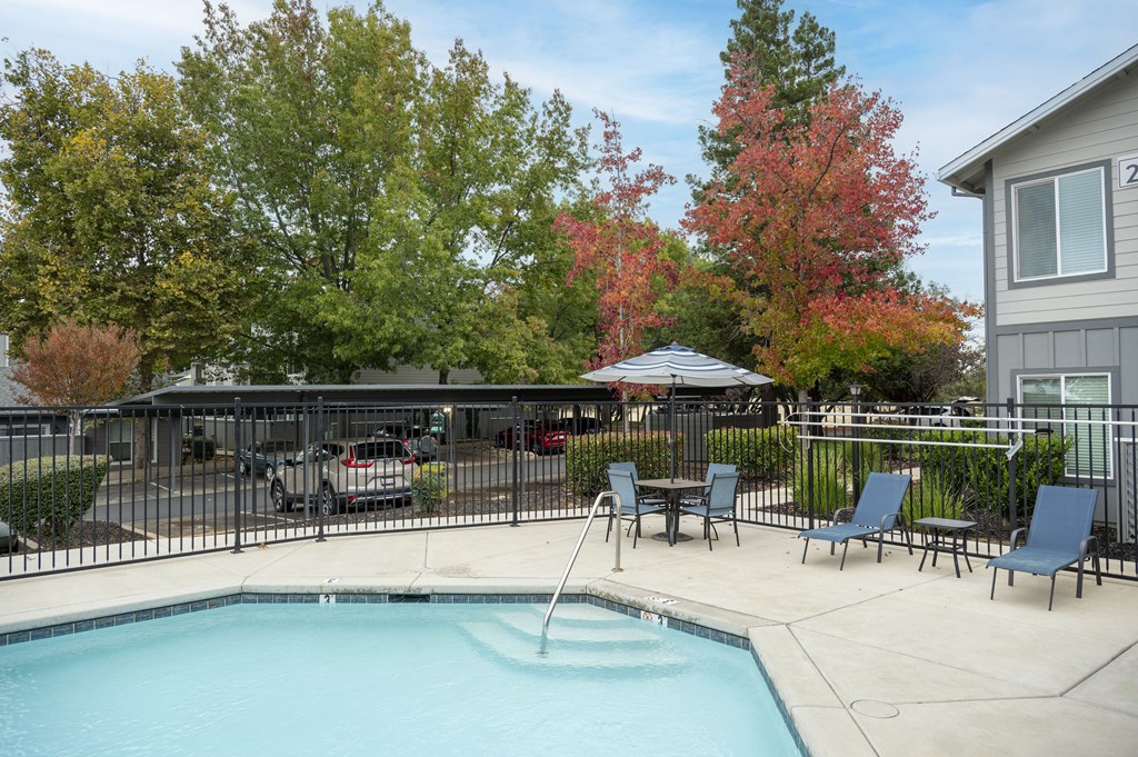 A pool surrounded by trees and chairs with a house in the background at Sierra Oaks Living Apartments, California 95682