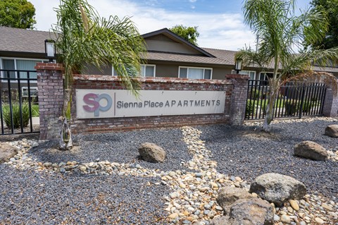 The image shows a sign for Sienna Place Apartments in front of a gated entrance.