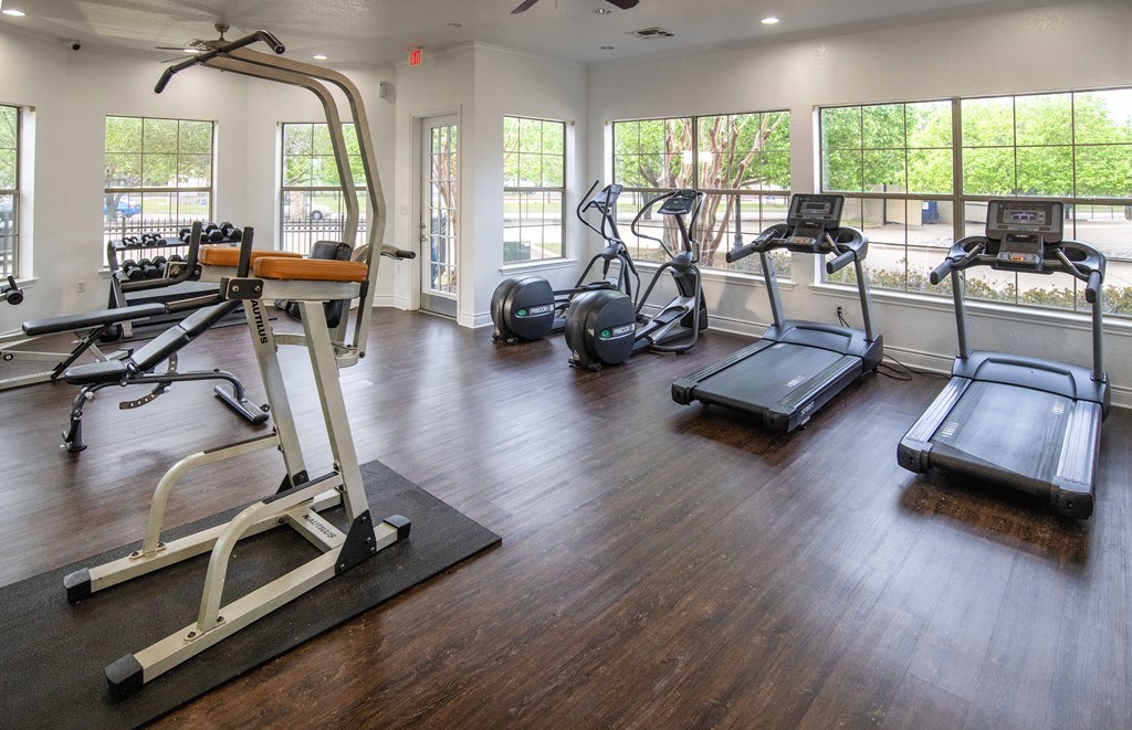 A gym with a variety of equipment including treadmills, elliptical machines, and a weight bench.
