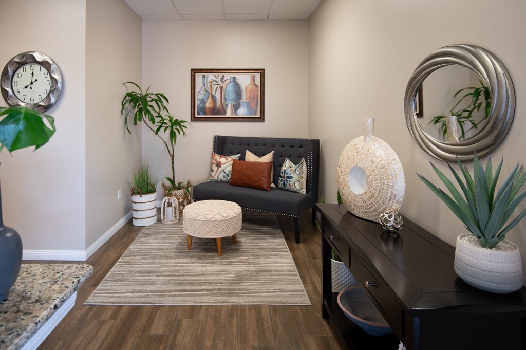 A living room with a couch, a rug, a plant, and a clock on the wall.