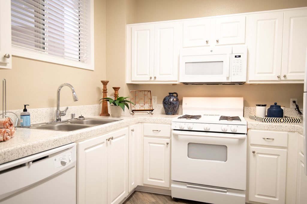 A white kitchen with a stove, sink, and cabinets.