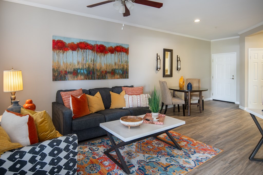 A living room with a grey couch, a painting of red flowers, and a rug with a geometric pattern.