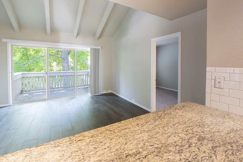 A room with a large bed and a balcony with a view of trees.
