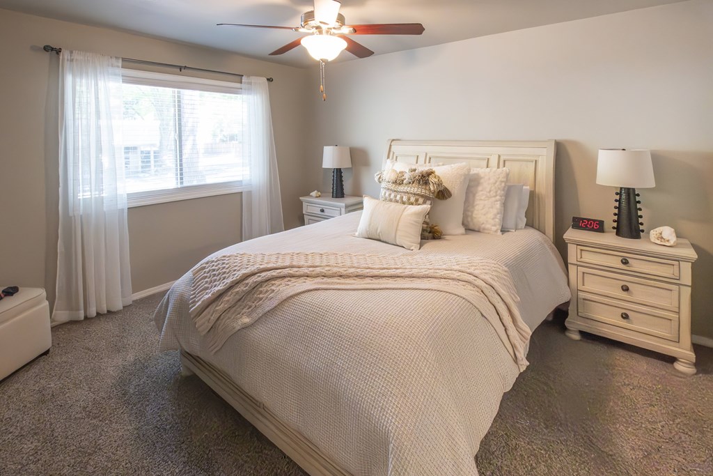 A bedroom with a large bed, a nightstand, and a window with curtains.