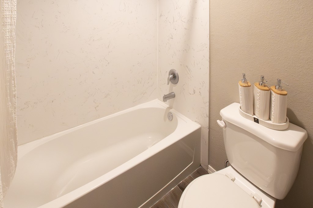 A white toilet with a toilet paper holder with four rolls of toilet paper.