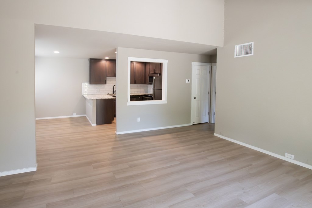A spacious room with wooden flooring and a kitchen area in the background.