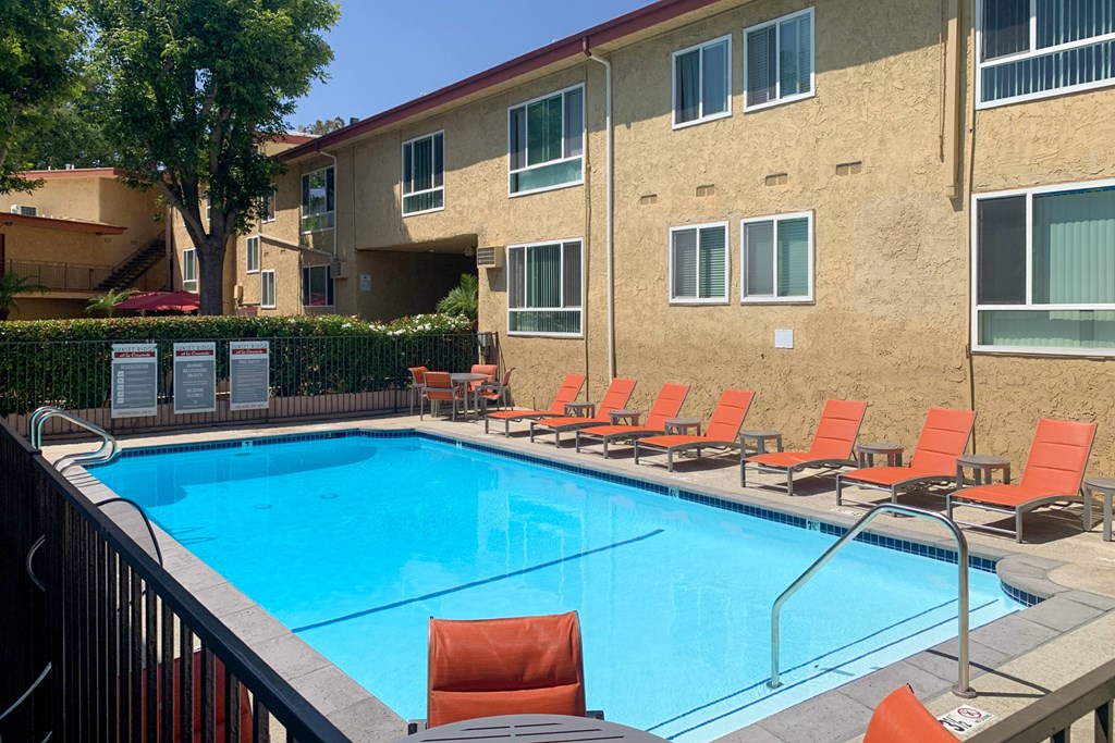 A pool surrounded by orange chairs and apartment buildings.