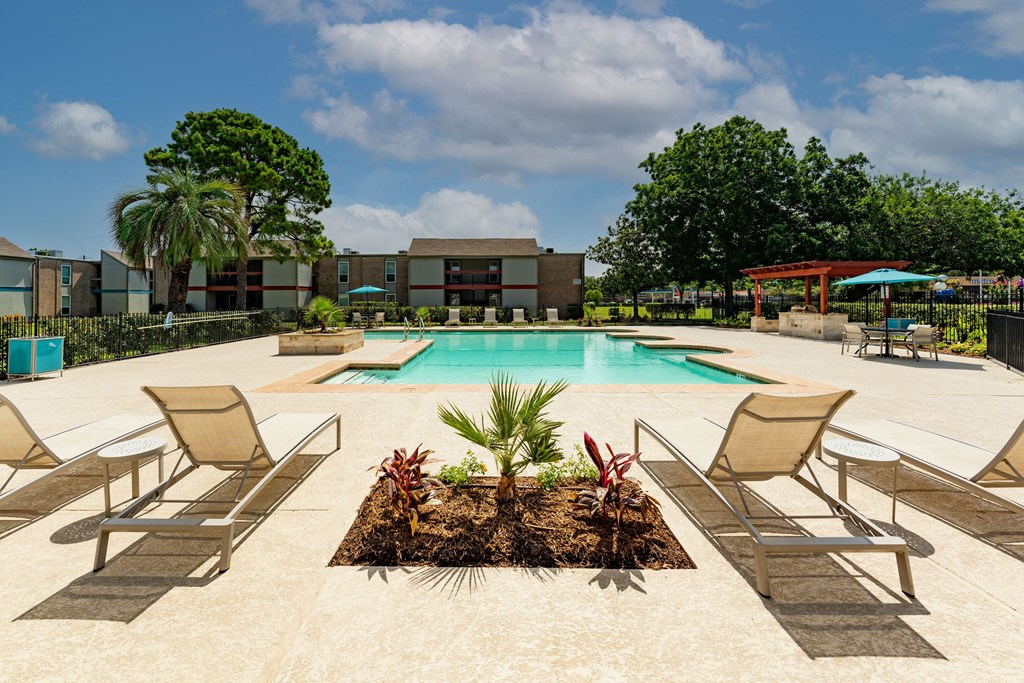 A pool surrounded by chairs and plants with a building in the background.