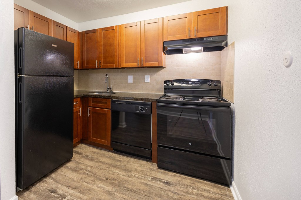 A black refrigerator is in a kitchen with wooden cabinets.