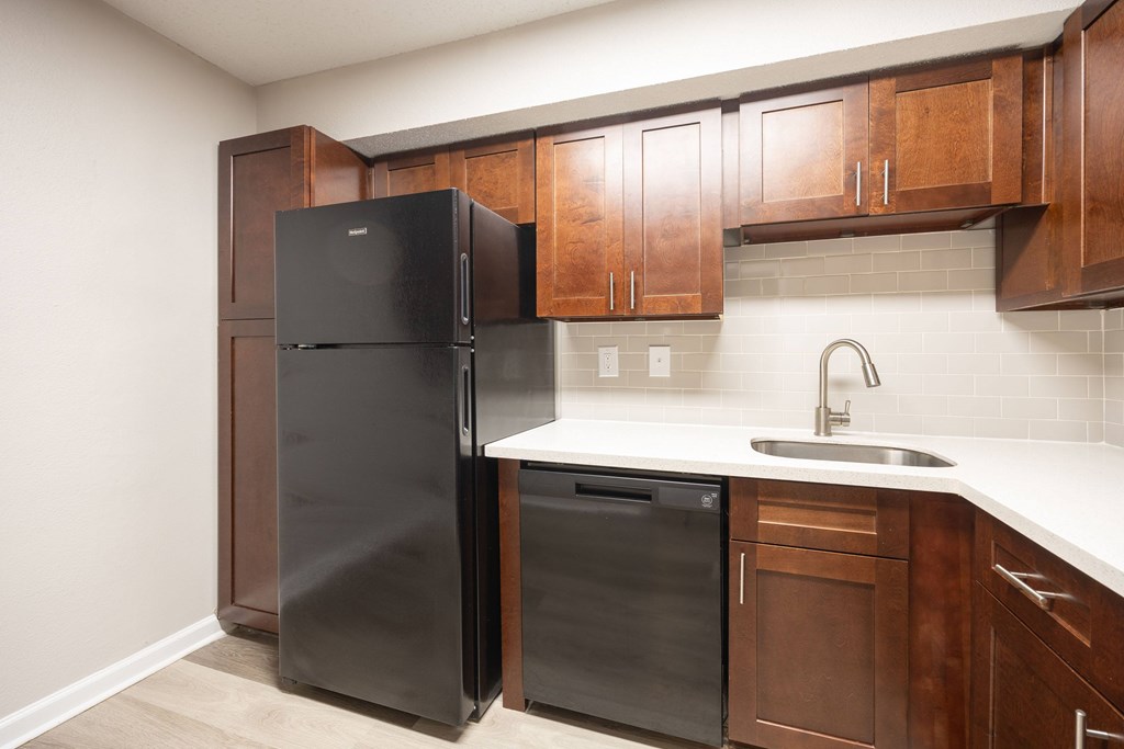 A black refrigerator and dishwasher in a kitchen with wooden cabinets.