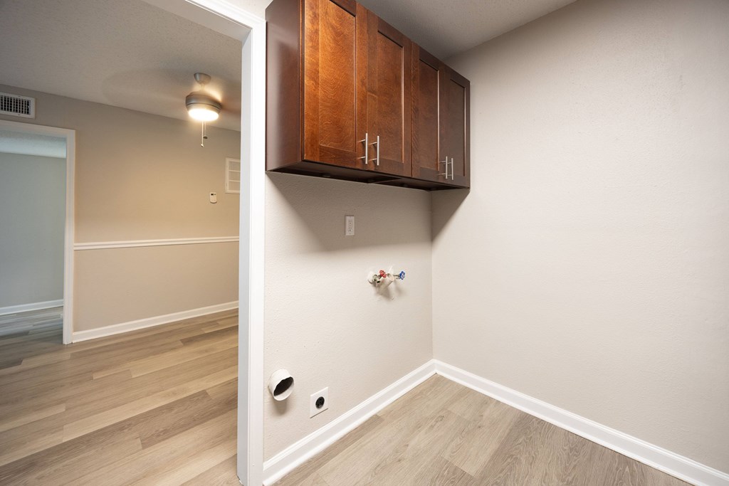 A room with wooden floors and a white wall with a brown cabinet above it.