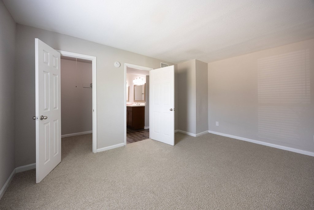 A room with carpeted floors and white walls with three open doors.