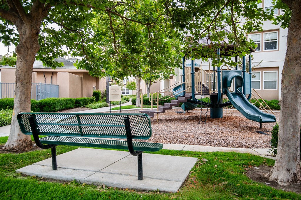 A green park bench sits in front of a playground.