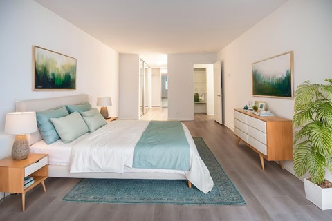 A bedroom with a bed, nightstand, and a plant.