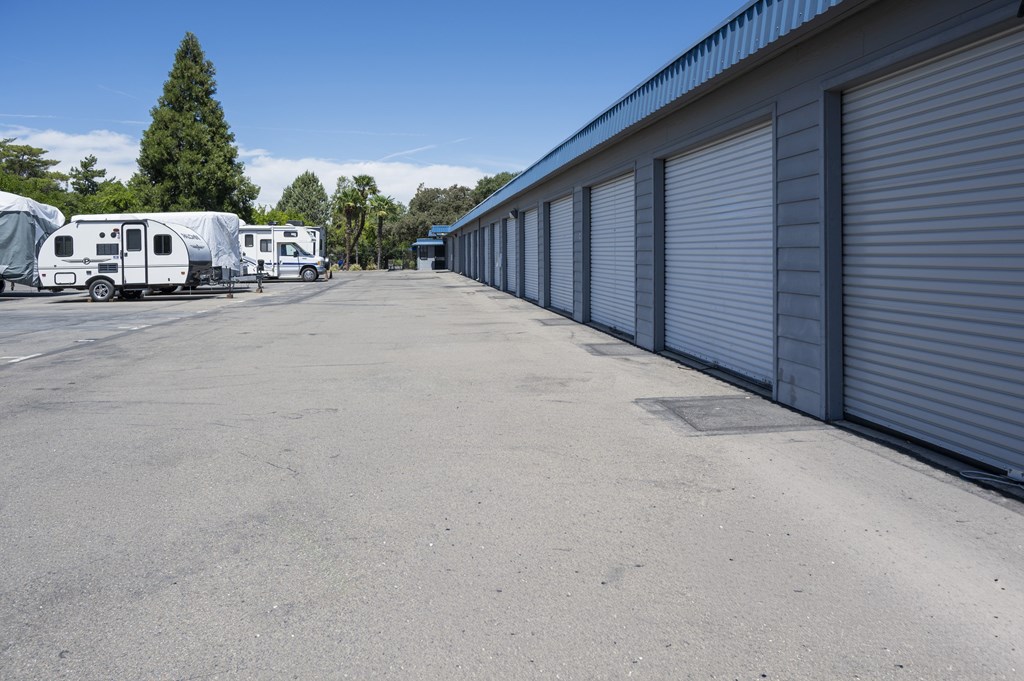 A parking lot with a row of grey storage units and a few parked RVs.
