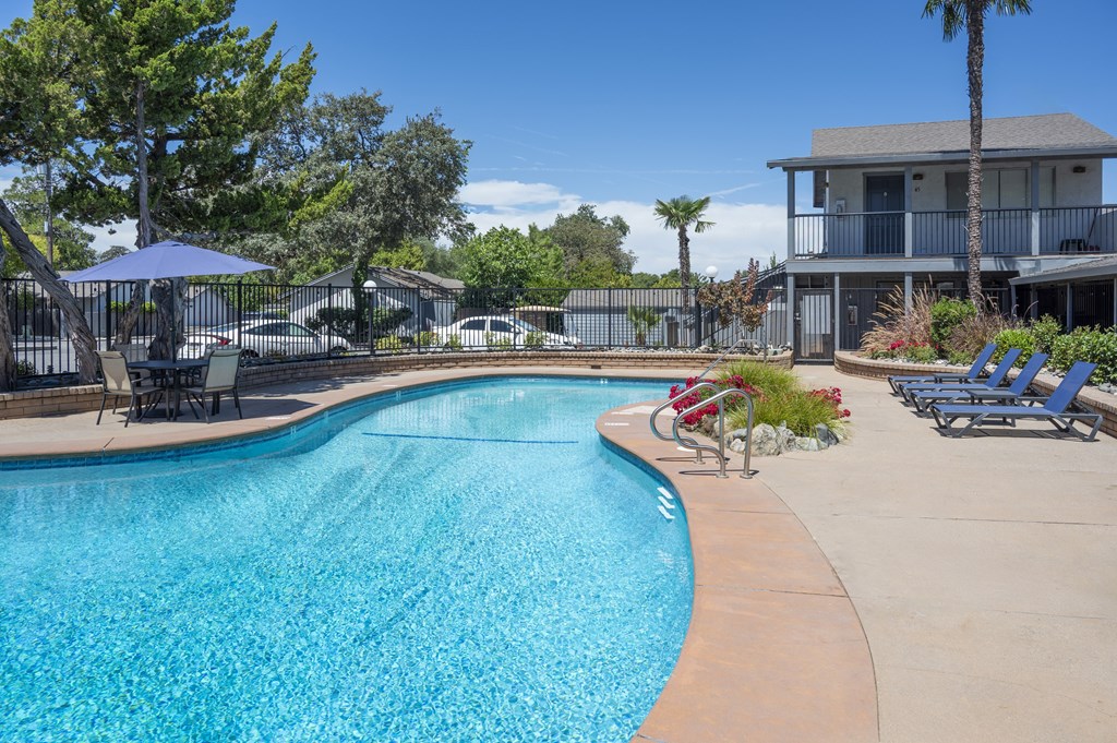 A swimming pool surrounded by a concrete patio and a white fence.