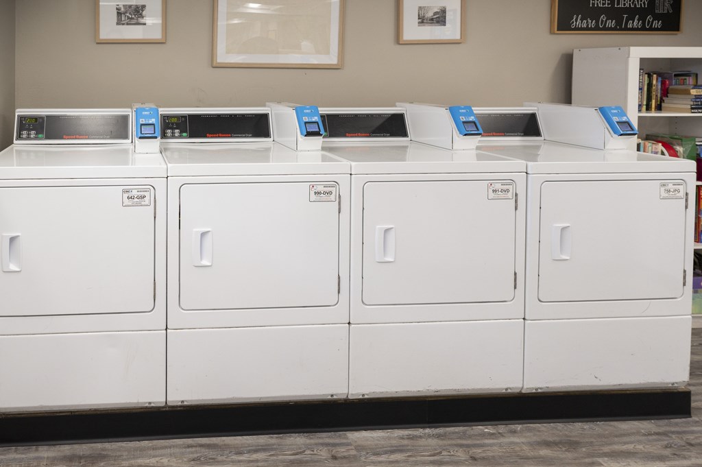 A row of white washing machines are lined up in a laundromat.