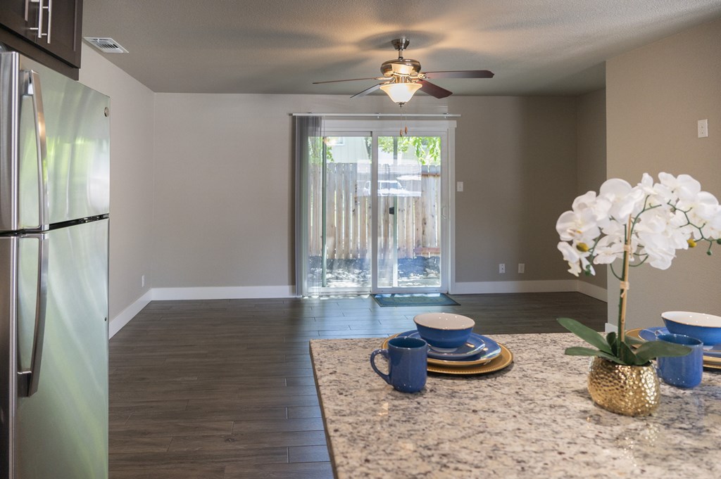 A kitchen with a refrigerator, a ceiling fan, and a dining table set with blue dinnerware.