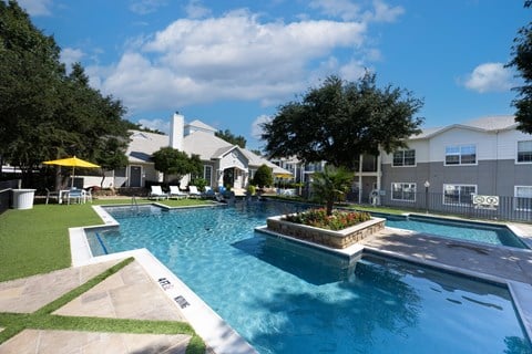 A large swimming pool with a small waterfall and a hot tub.