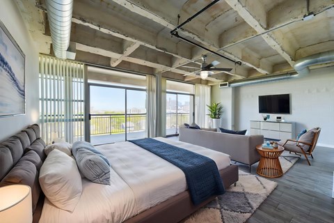 A bedroom with a large bed and a balcony overlooking the city.
