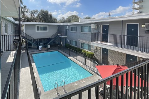 A pool surrounded by a black fence and red umbrellas.