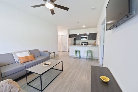 A modern living room with a grey sofa, a glass coffee table, and a flat screen TV mounted on the wall.
