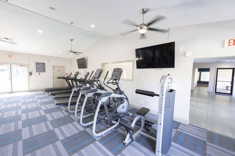 A gym with a row of treadmills and a television.