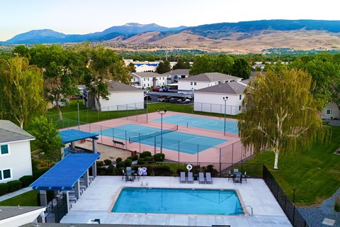 A tennis court is surrounded by a pool and a fence.
