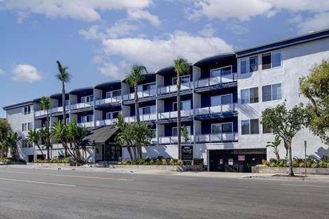 A modern apartment building with balconies and palm trees in front.
