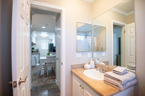 A bathroom with a sink, mirror, and a view of the dining area.
