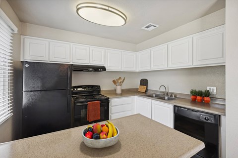 A kitchen with a black refrigerator, white cabinets, and a bowl of fruit on the counter.