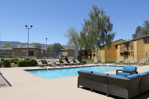 A pool with a couch and chairs in the foreground and a building in the background.