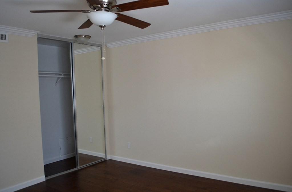 View of bedroom with wood look flooring, sliding glass mirror closet, and ceiling fan with light fixture