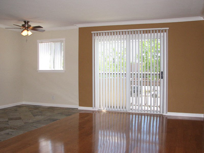 View of living room with tile and wood flooring, sliding glass door leading to private patio/balcony, and ceiling fan