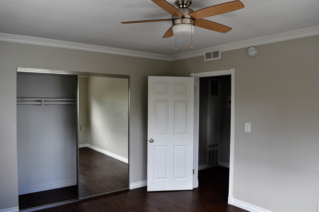 View of bedroom with wood look flooring, sliding glass mirror closet, and ceiling fan