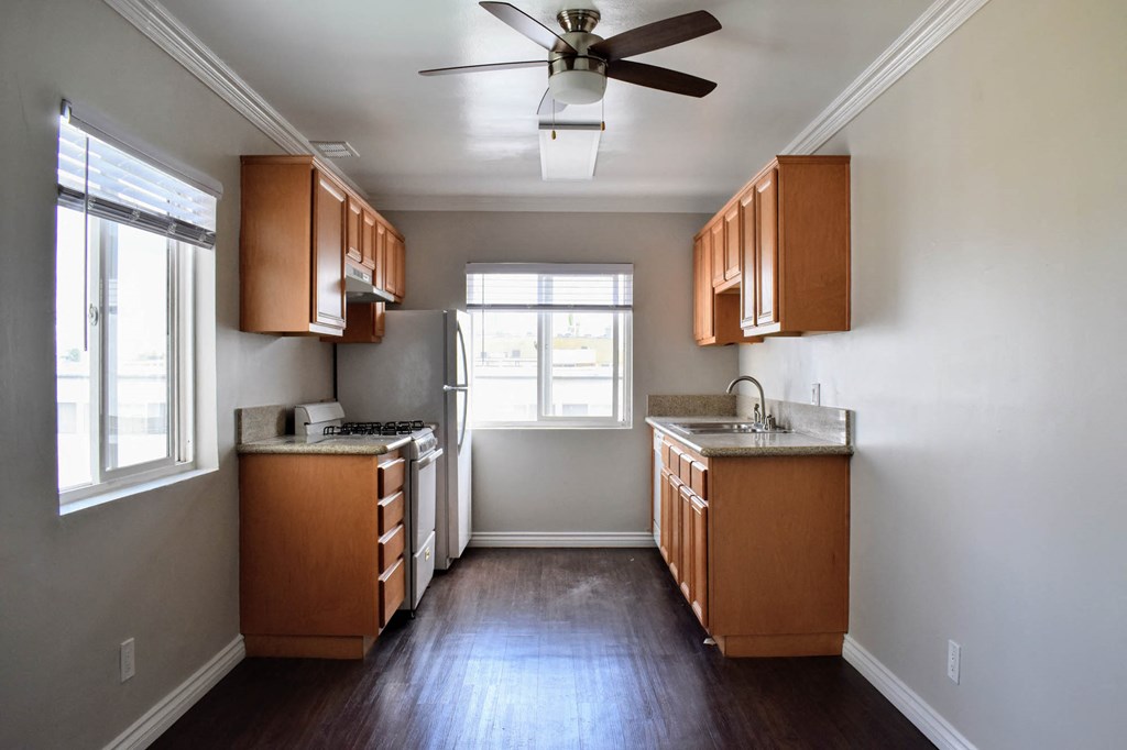 View of well lit kitchen with ceiling fan and light fixture, wood look flooring, windows, and brown cabinets