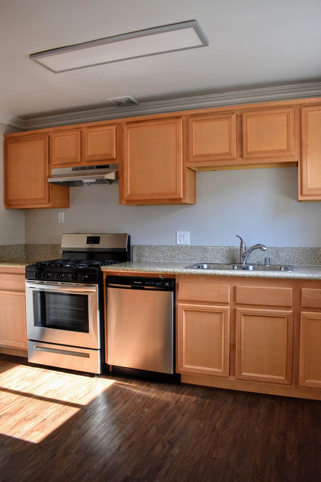 View of kitchen with wood look flooring, brown cabinets, stainless appliances, and inlaid sink