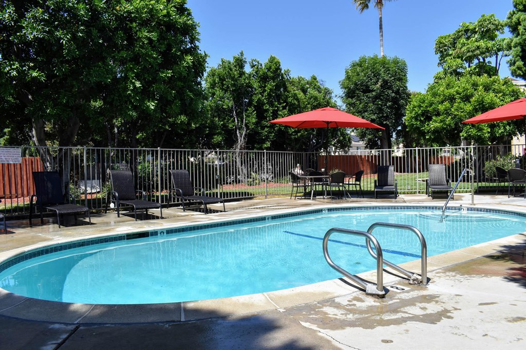 View of gated pool with lounge chairs and seating areas under umbrellas