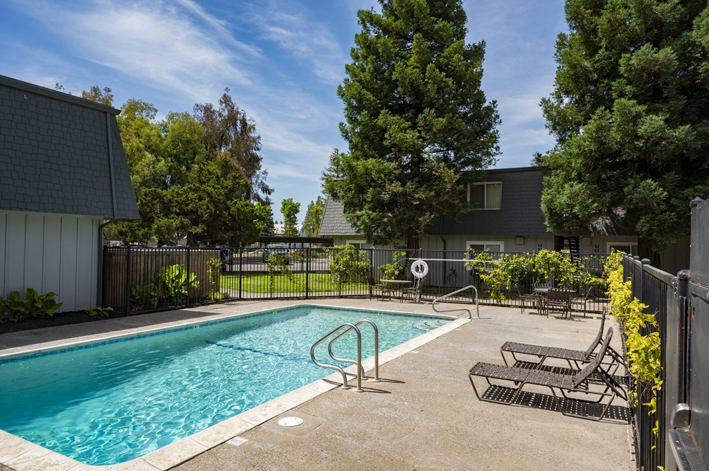 View of gated community pool area with seating and lounge chairs